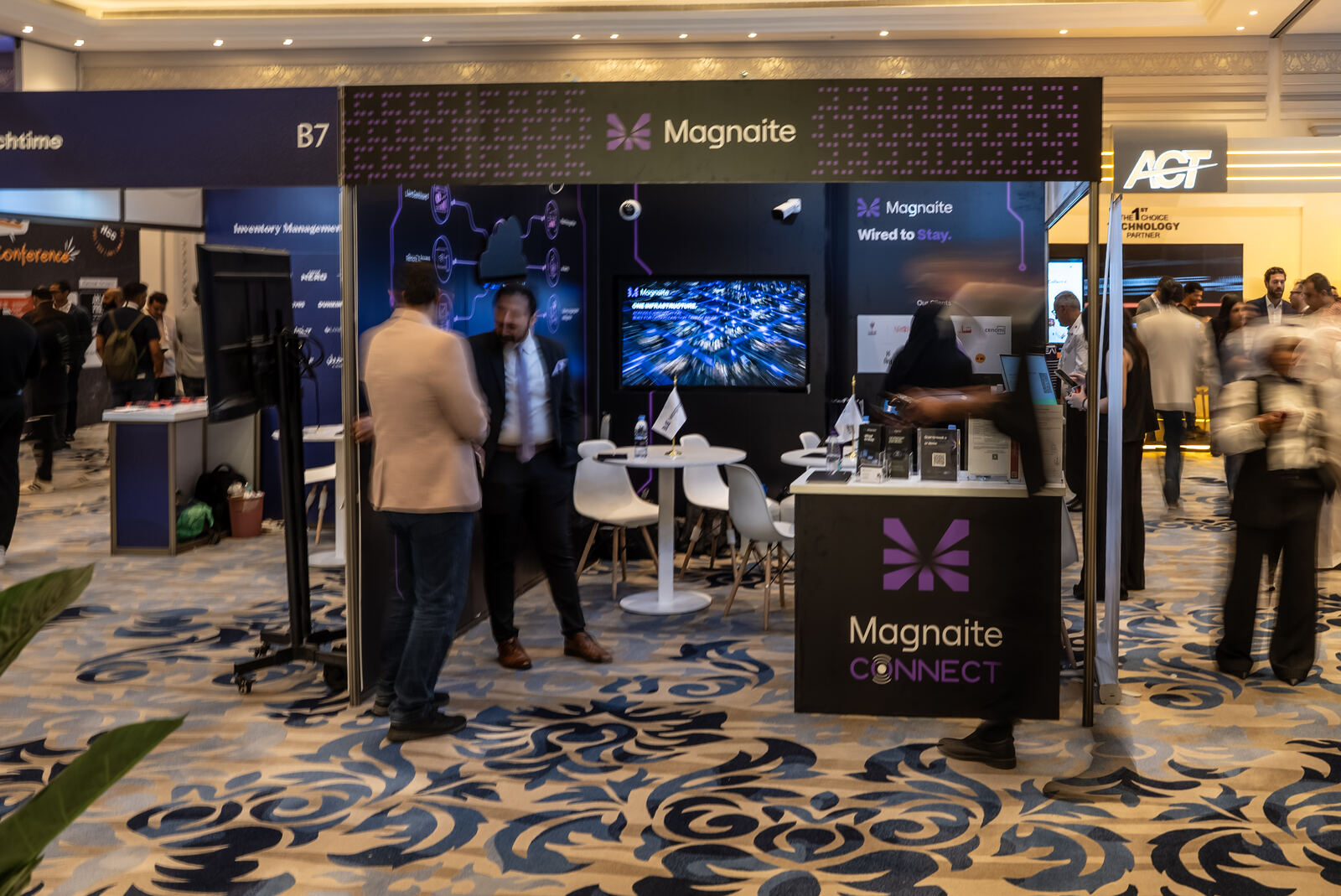 Wide view of the booth floor with visitors, screen displaying the 'One Infrastructure' animation.