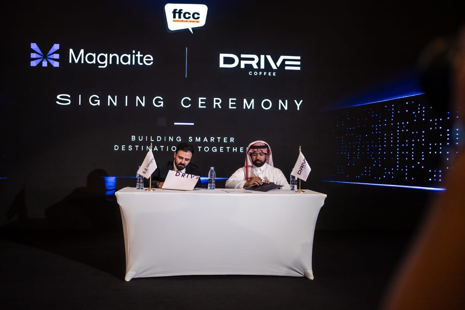 Magnaite and Drive Coffee representatives signing the partnership agreement on stage.